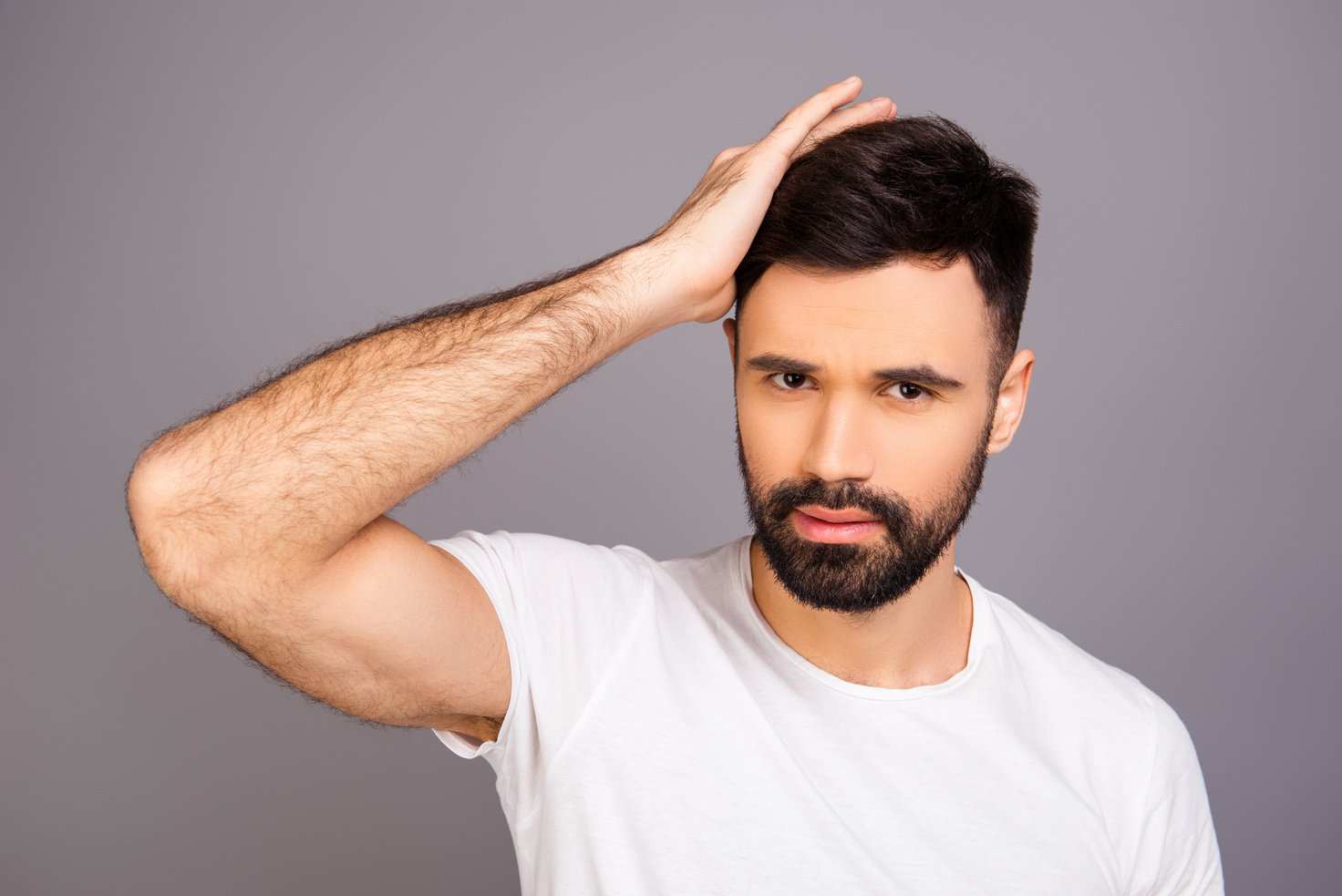 Handsome cheerful young man combing his hair with fingers